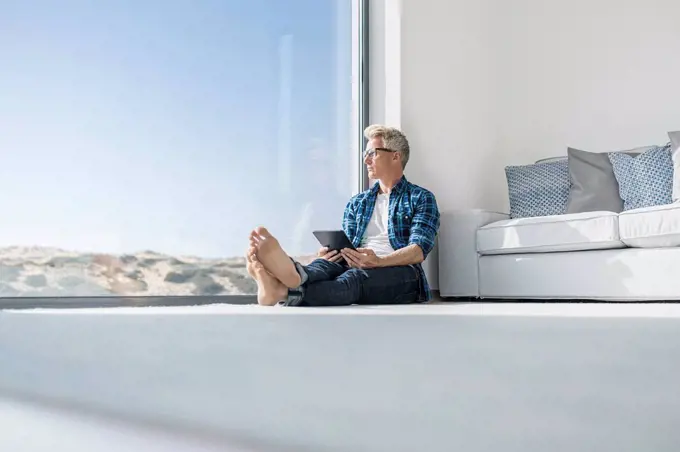 Casual businessman sitting in front of window in modern home holding tablet