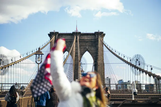 Woman standing on Brooklyn Bridge holding the American flag, New York, United States