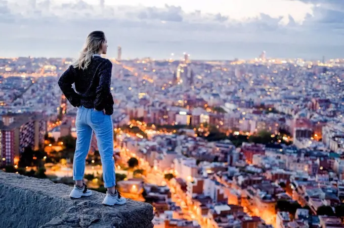 Rear view of young woman standing above the city at dawn, Barcelona, Spain