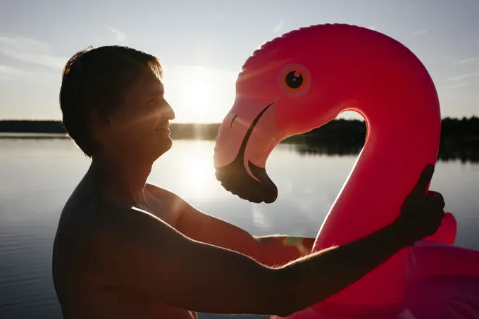 Young man with flamingo pool float at sunset