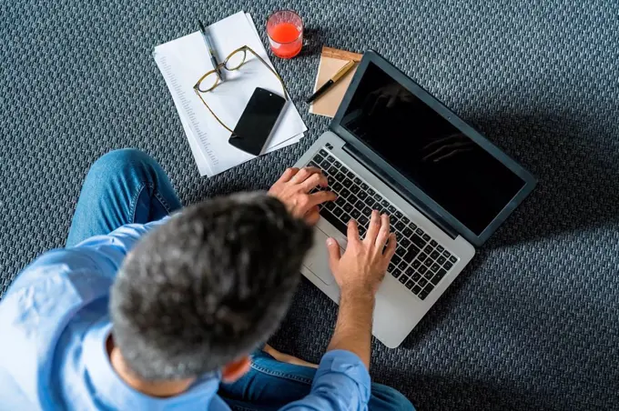 Man sitting on the floor at home using laptop, top view