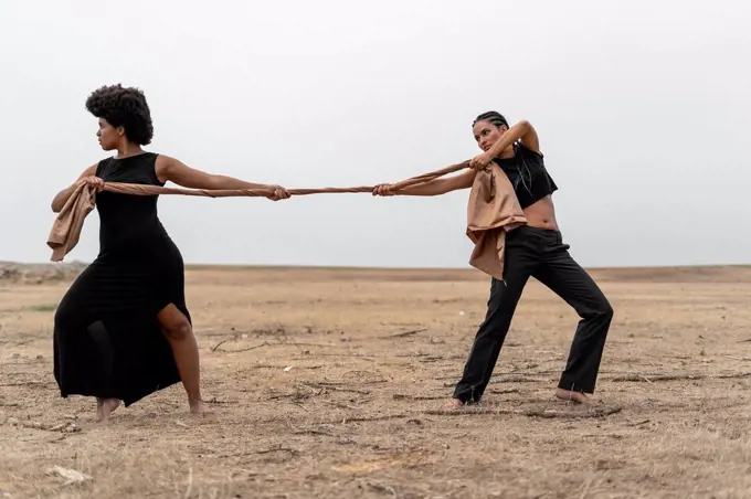 Two women pulling a cloth in bleak landscape