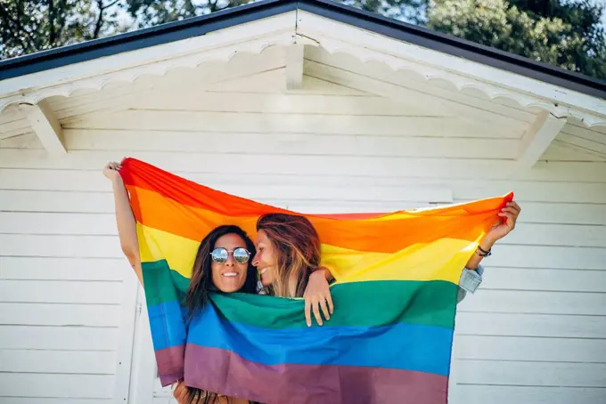 Two smiling women holding up a rainbow flag