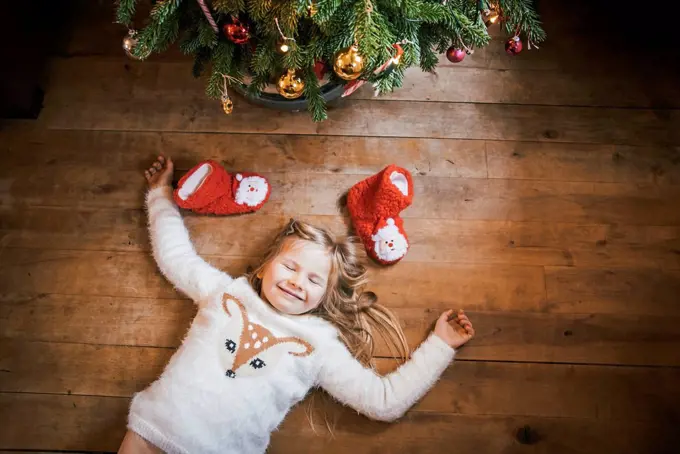 Smiling girl with closed eyes lying under the Christmas tree