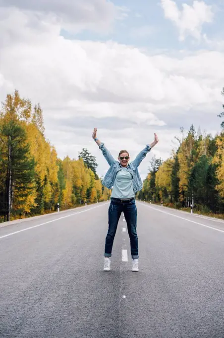 Happy woman standing on empty country road in autumn