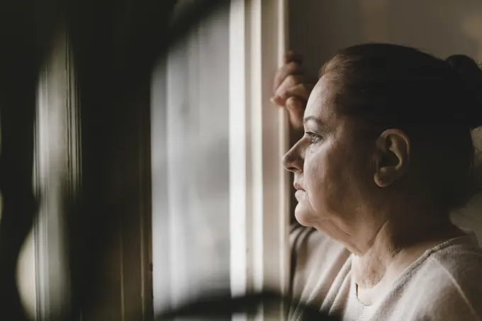 Serious senior woman looking out of window at home