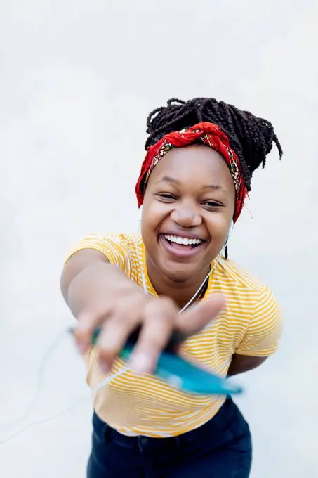 Portrait of happy young woman listening music with headphones and earphones in front of white wall