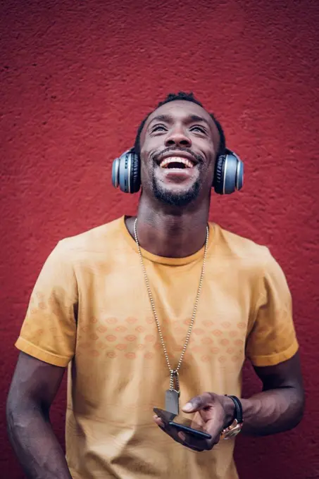 Portrait of happy man with headphones and smartphone looking up