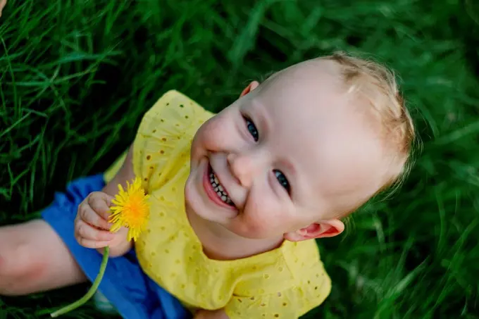 Portrait of happy little girl with dandelion sitting on a meadow