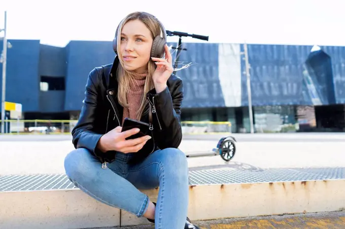 Portrait of young woman listening music with smartphone and headphones, Barcelona, Spain