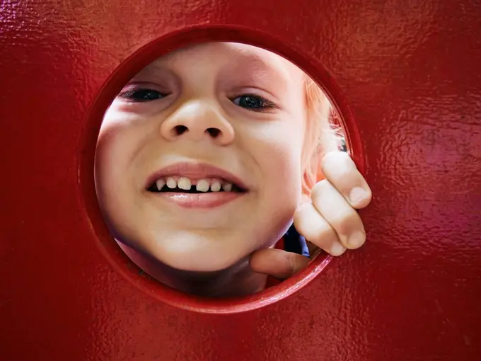 Portrait of smiling little boy looking through hole on playground