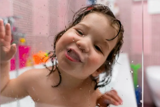 Portrait of happy little girl in bathtub behind glass pane