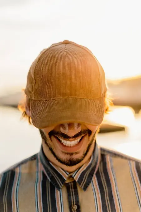 Laughing man wearing baseball cap at sunset