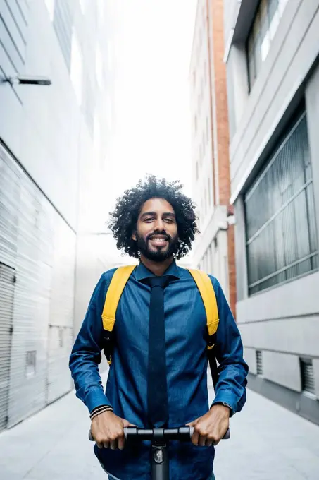 Portrait of smiling young man with backpack on E-Scooter after work