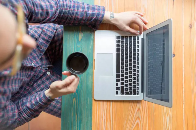 Man wearing pyjama sitting with coffee cup in front of laptop