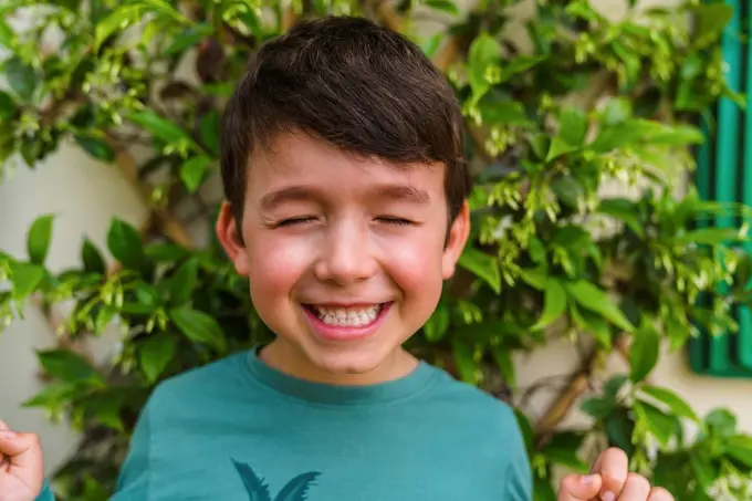 Portrait of grinning little boy on balcony with eyes closed