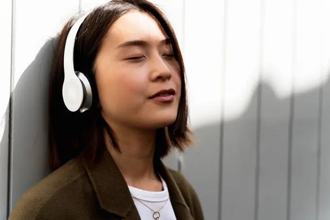 Relaxed young woman with closed eyes listening to music with headphones