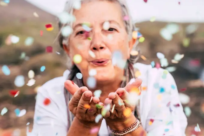 Senior woman blowing confetti outdoors