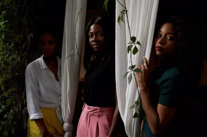 Portrait of three women standing between curtains