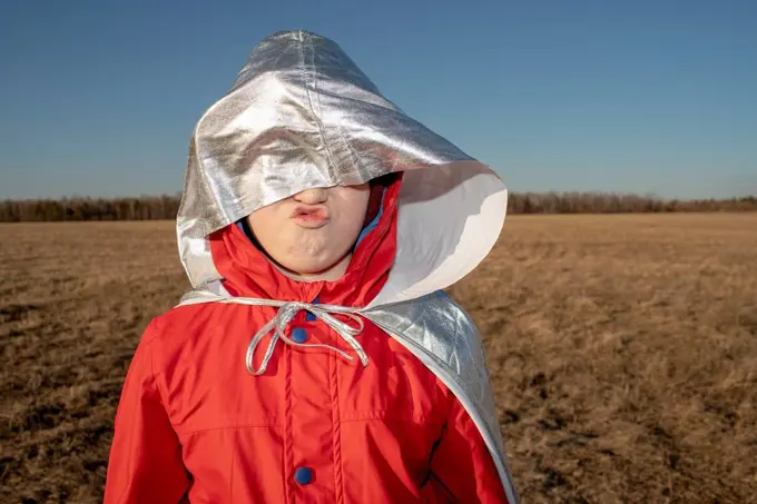 Hood of superhero costume covering boy's face in steppe landscape