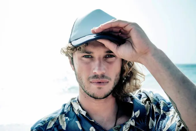 Portrait of bearded blond man wearing baseball cap in front of the sea