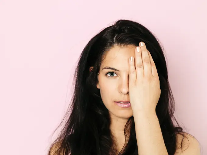 Portrait of young woman with black hair, eye covered in front of pink background