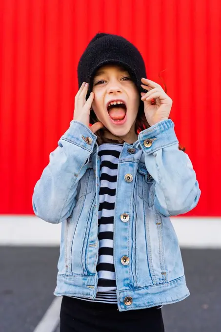 Portrait of screaming little girl wearing denim jacket and black cap