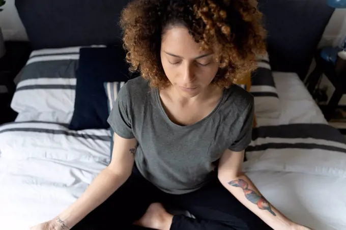 Woman practicing yoga, sitting on bed, meditating