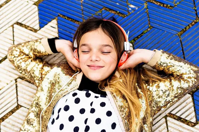 Portrait of happy girl wearing golden sequin jacket listening music with headphones