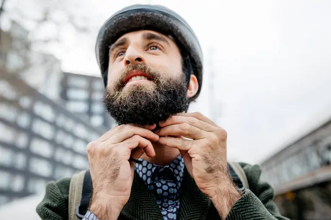 Portrait of man putting on bicycle helmet in the city