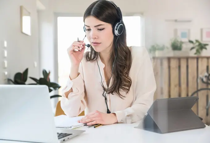 Young woman sitting at table at home wearing a headset