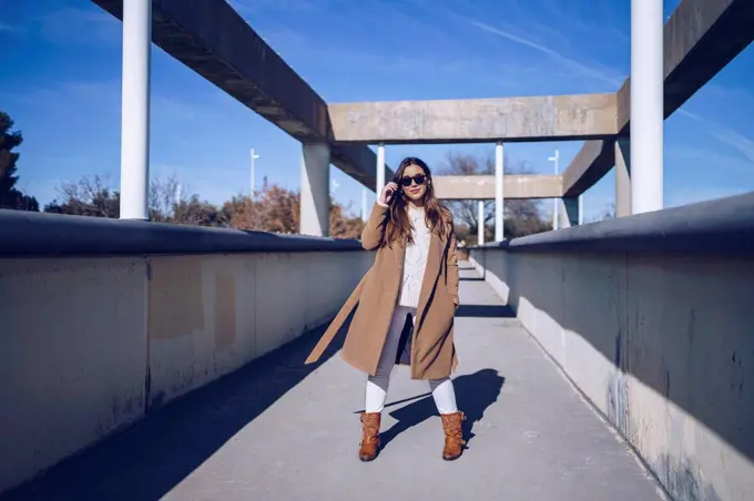 Young woman wearing coat and sunglasses standing on a bridge