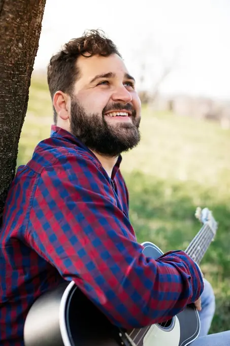 Portrait of smiling man with guitar at a tree on a meadow