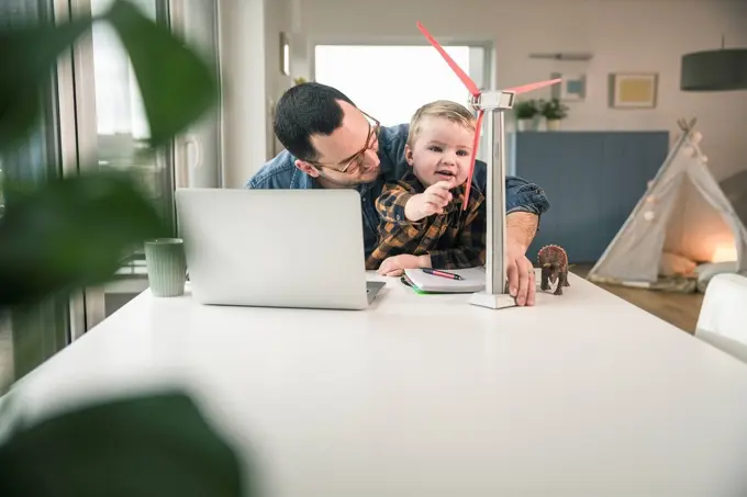 Father and son at home with wind turbine model on table