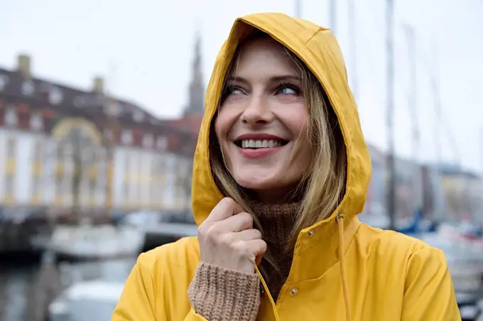 Denmark, Copenhagen, portrait of happy woman at city harbour in rainy weather