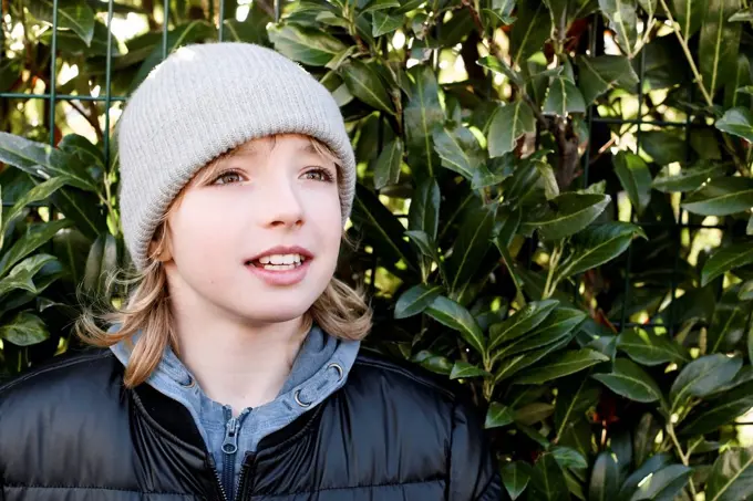 Portrait of boy wearing wooly hat at a hedge