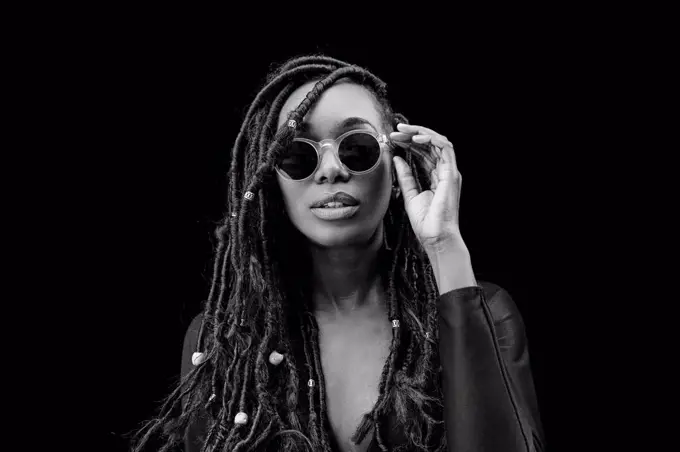 Portrait of woman with dreadlocks wearing sunglasses in front of black background