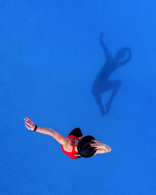 Jumping young woman and her shadow on blue background, top view