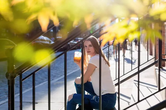 Young woman exploring New York City, sitting on stairs, drinking coffee