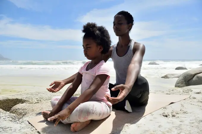 Mother with daughter doing a yoga exercise on the beach