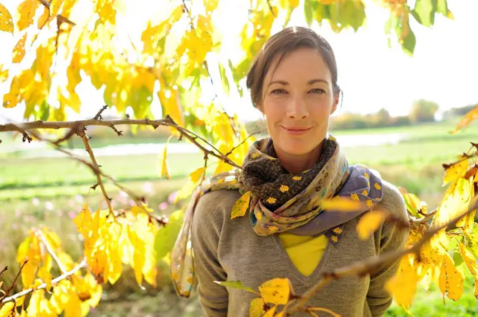 Portrait of woman at twigs with autumn leaves looking at camera