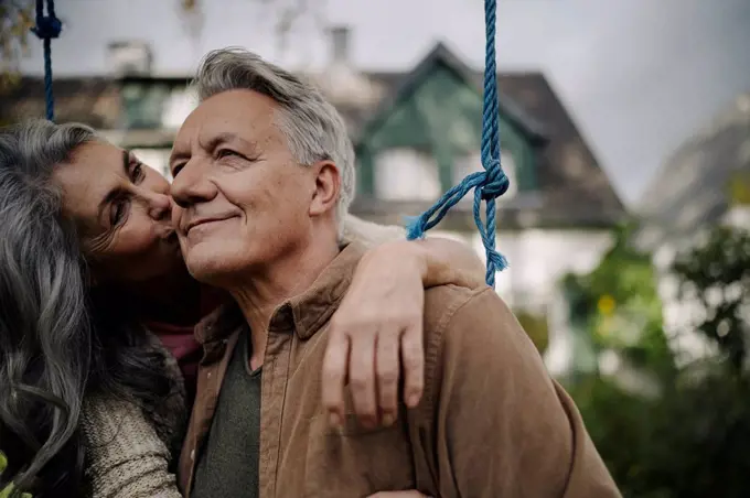 Happy woman hugging an kissing senior man on a swing in garden