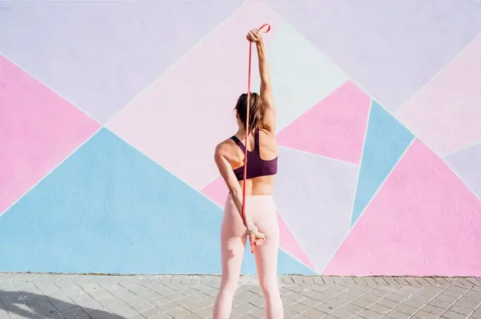 Rear view of female athlete with fitness band in front of colorful wall