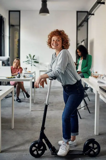 Portrait of a smiling businesswoman with kick scooter in office