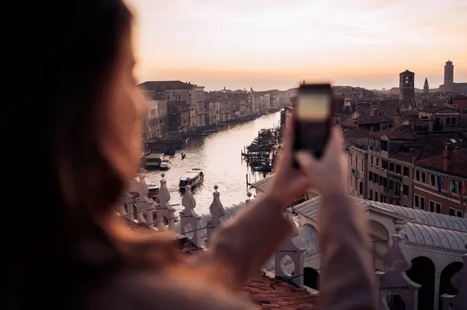 Young woman taking cell phone picture on a balcony above the city of Venice, Italy