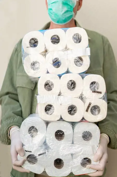 Man with face mask and protective gloves, holding packets of toilet paper