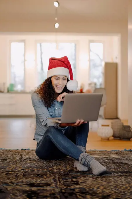 Woman with Santa hat looking for presents online, using laptop