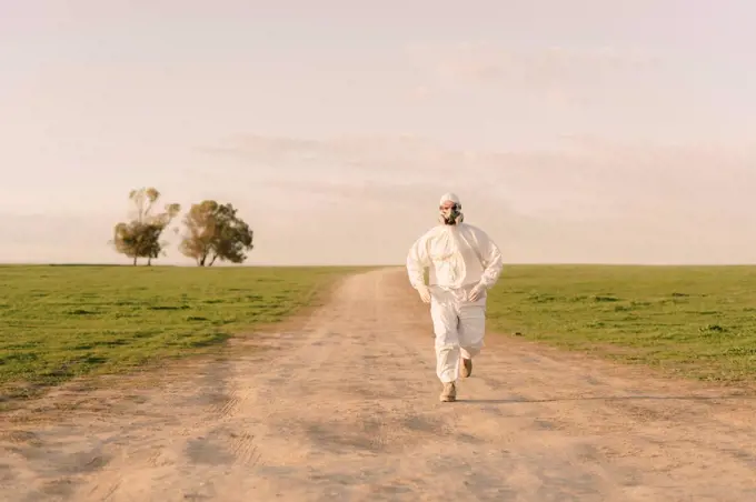 Man wearing protective suit and mask running on dirt track in the countryside