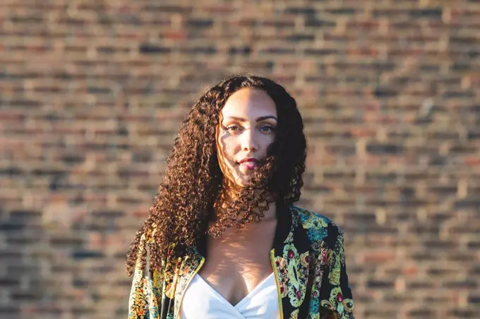 Portrait of young woman with curly hair in front of brick wall