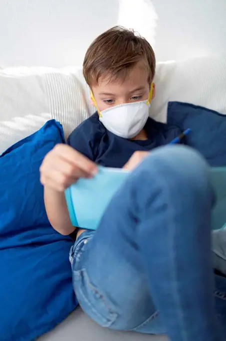 Boy with mask is in his room doing homework at home during the corona crisis